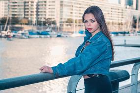 Young girl with make-up posing near the railing on the coast of the river, at background with the buildings
