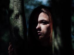 Portrait of the woman in light and darkness, hiding behind the tree