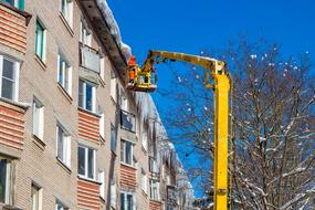 Person knocks icicles off the building, with the crane, in the winter