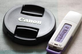 Close-up of the shiny, black "Canon" camera, and blue and violet USB disk, in light