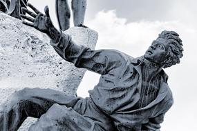 Black and white photo of the bronze statue of the man, at background with the sky with clouds