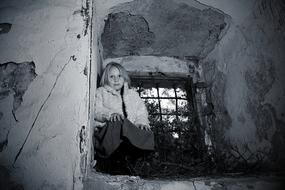 Black and white photo of the cute girl sitting at the old window