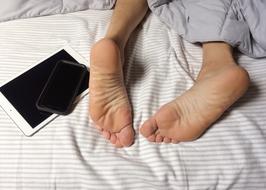 feet of a man next to a tablet on the bed