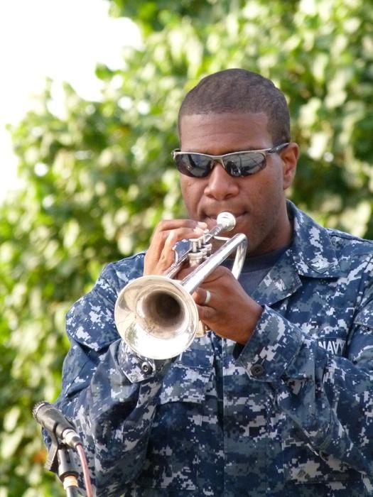 Man, playing on the shiny trumpet, near the green plants in light