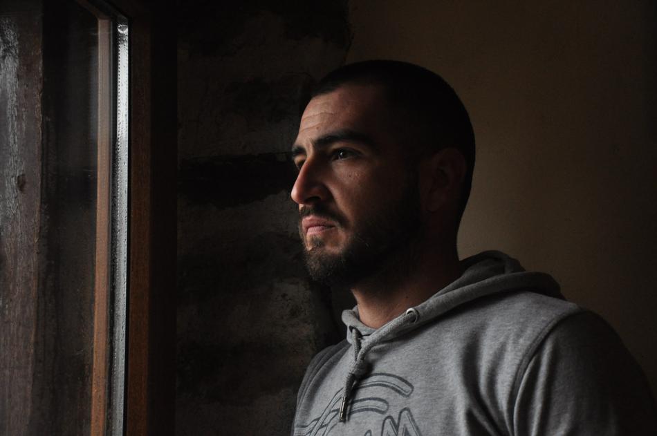 Profile portrait of the man with beard, in grey hoodie, among the darkness