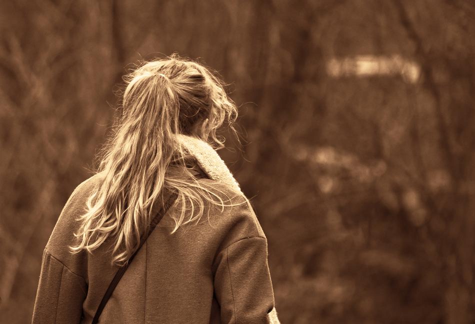 Back view of the blonde girl in coat, near the plants