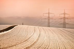 Beautiful, snowy landscape of the fields with power poles and a person, at colorful sunset, in the winter