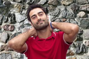 Portrait of the young man with beard, in red shirt, at background with the stone wall