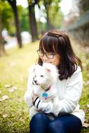 Smiling, Asian girl with glasses holding beautiful and cute, white, fluffy dog