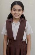 Cute, smiling girl of the Indian school, in the school dress, near the wall