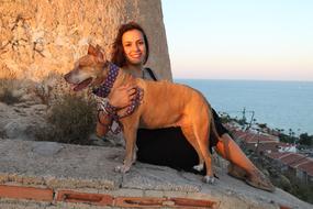 Smiling girl posing with the cute and beautiful dog, on the cost of the water, at colorful sunset