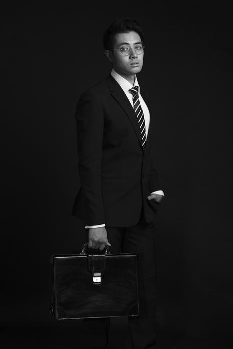 Black and white photo of the man in suit, and with the suitcase, at black background