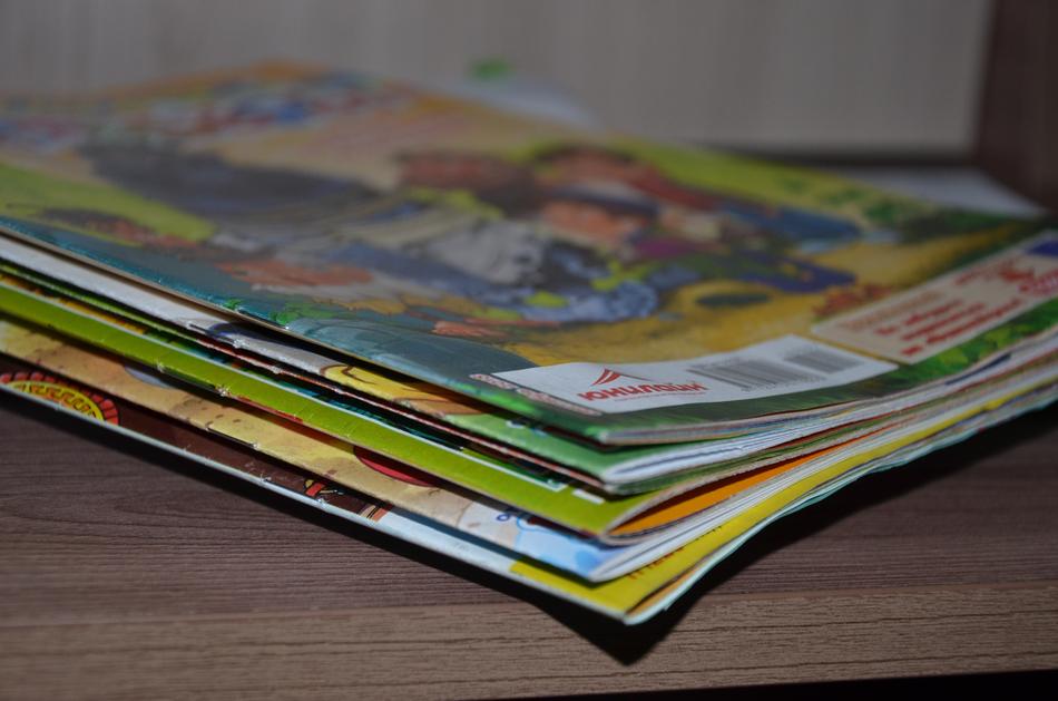 Close-up of the pile of the colorful magazines, in light and shadow, on the wooden surface
