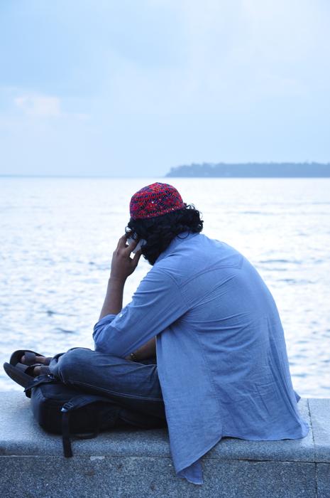 Back view of the man in cap, sitting on the coast of water in Mumbai, India