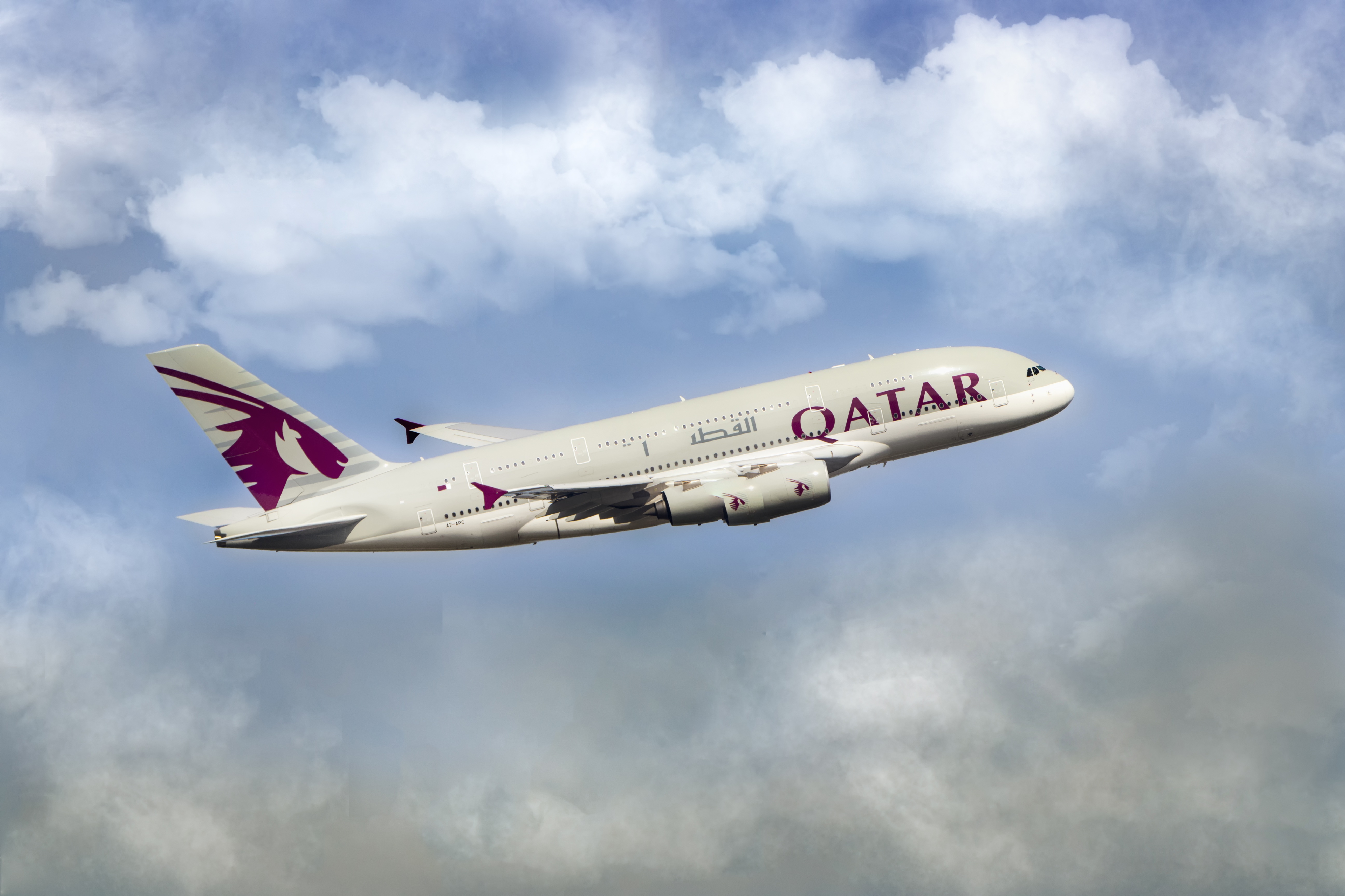 Side view of the flying, red and white “Qatar Airlines” airplane among