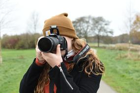 Portrait of the photographer girl in hat, with the camera, among the plants on landscape