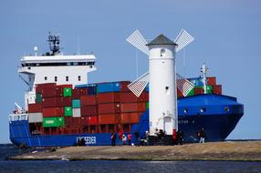 Colorful ship with the containers, near the port with white lighthouse and people, in Poland, at blue sky on background