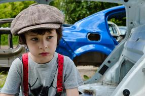 Portrait of the boy in cap, near the shiny, blue car and plants