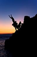 Silhouettes of the people on the rocks, near the water, at colorful and beautiful, gradient sunset