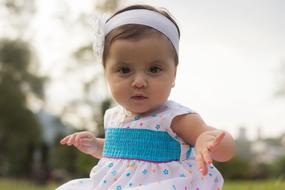 Portrait of the cute baby girl with headband, wearing colorful dress, among the plants