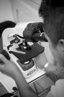 Black and white photo of the man, using microscope