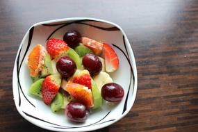 Beautiful fruit salad with cherries, strawberries, kiwi, orange and banana in the white and black bowl