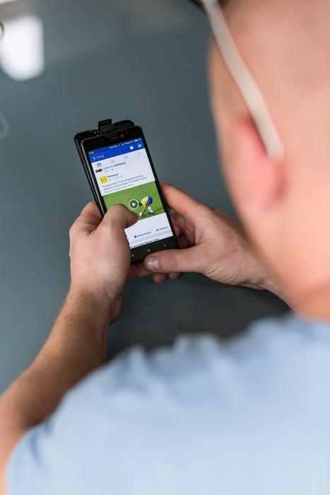 man holds phone with Facebook page on screen