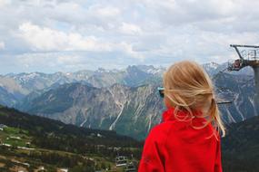 a girl in a red sweater stands on the top of a mountain