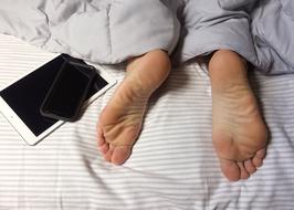 White tablet and black smartphone on the bed, near the feet of the sleeping person