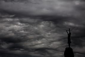 silhouette of a girl on a rock against gray clouds