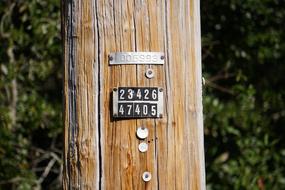 Black and white sign, with the numbers, on the wooden power pole, near the green trees
