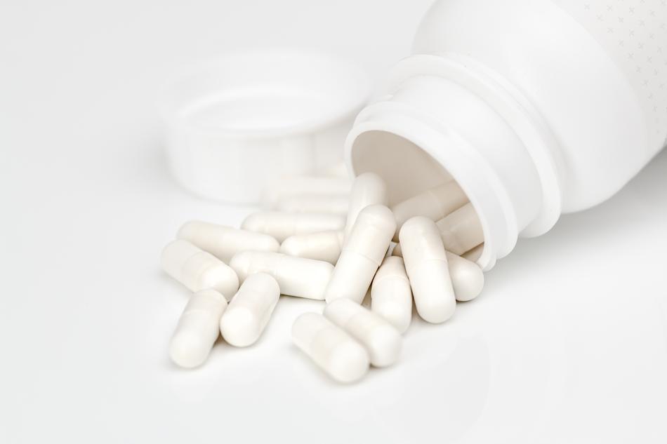 White pills, pouring out of the white bottle, on the white surface