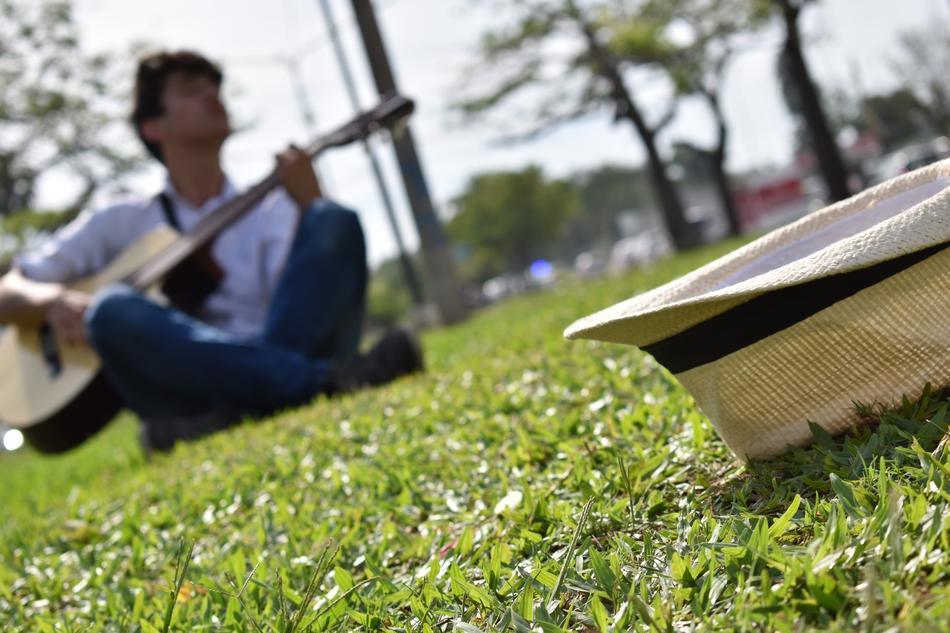 white hat in front of young man playing Guitar on lawn