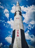 Low angle shot of the Saturn V rocket, with the USA flag, under the blue sky with clouds