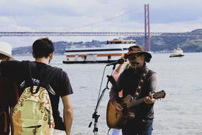 photo of man playing guitar and singing at coastline