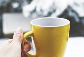 yellow coffee mug in hand against a background of white snow