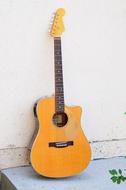 yellow wooden guitar against a white wall
