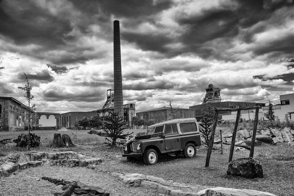 Black and white landscape with the car near the buildings, under the sky with clouds