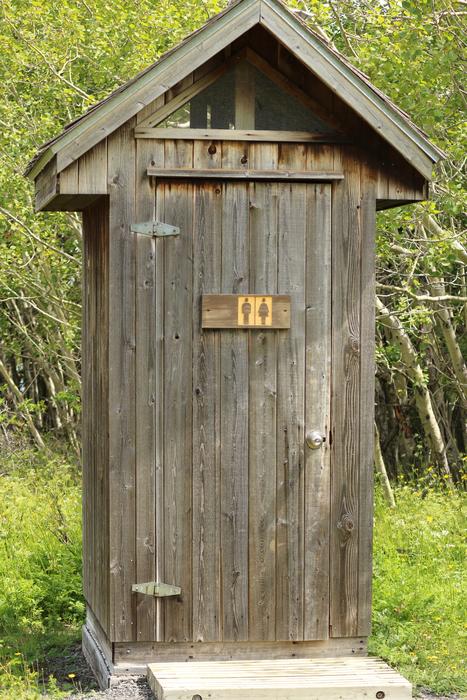 Wooden toilet with the sign, in sunlight, among the colorful plants